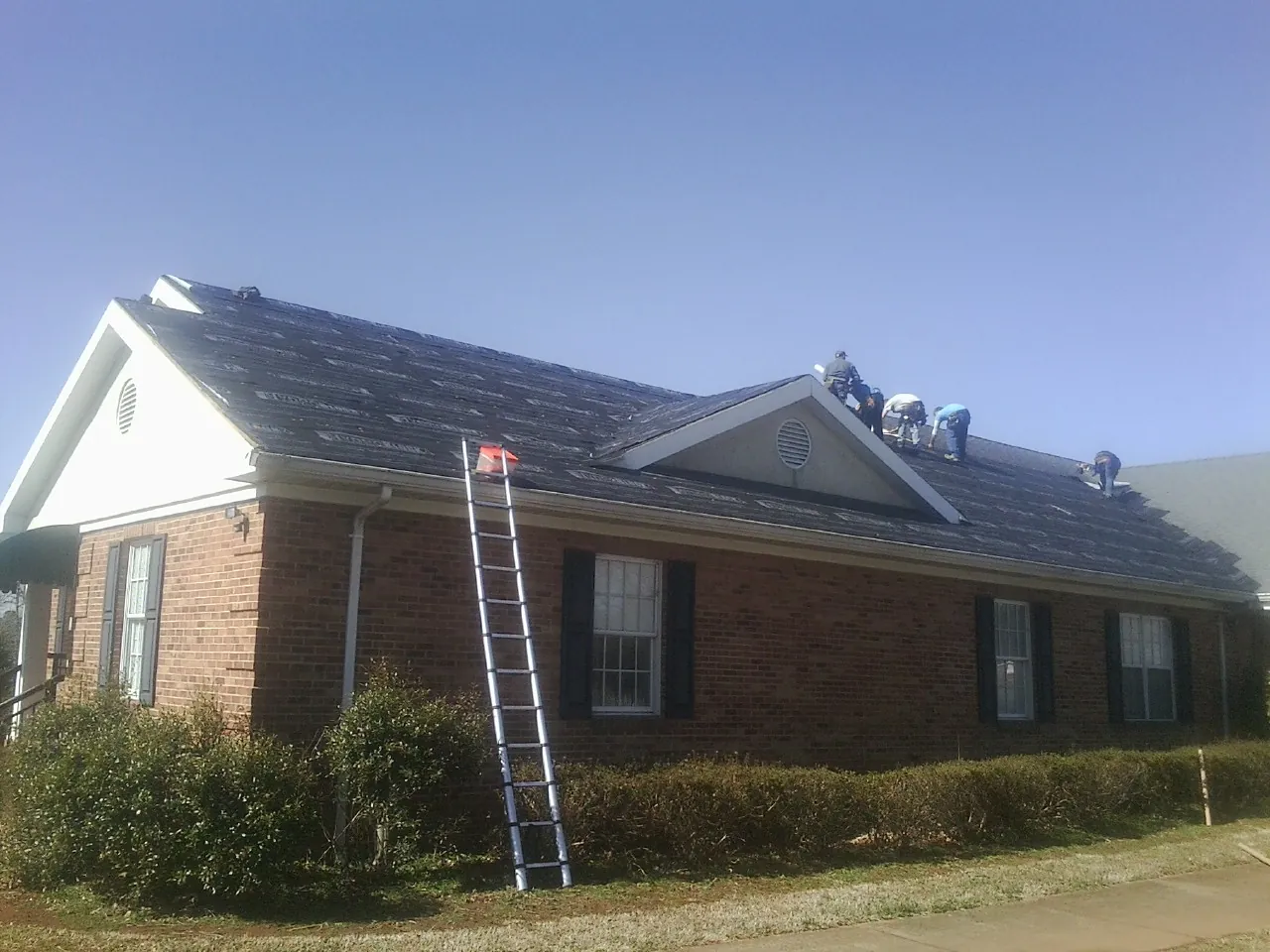 Crew tearing shingles off a brick ranch roof with a ladder set — Metal Roof Repair work by our crew in Plainsboro