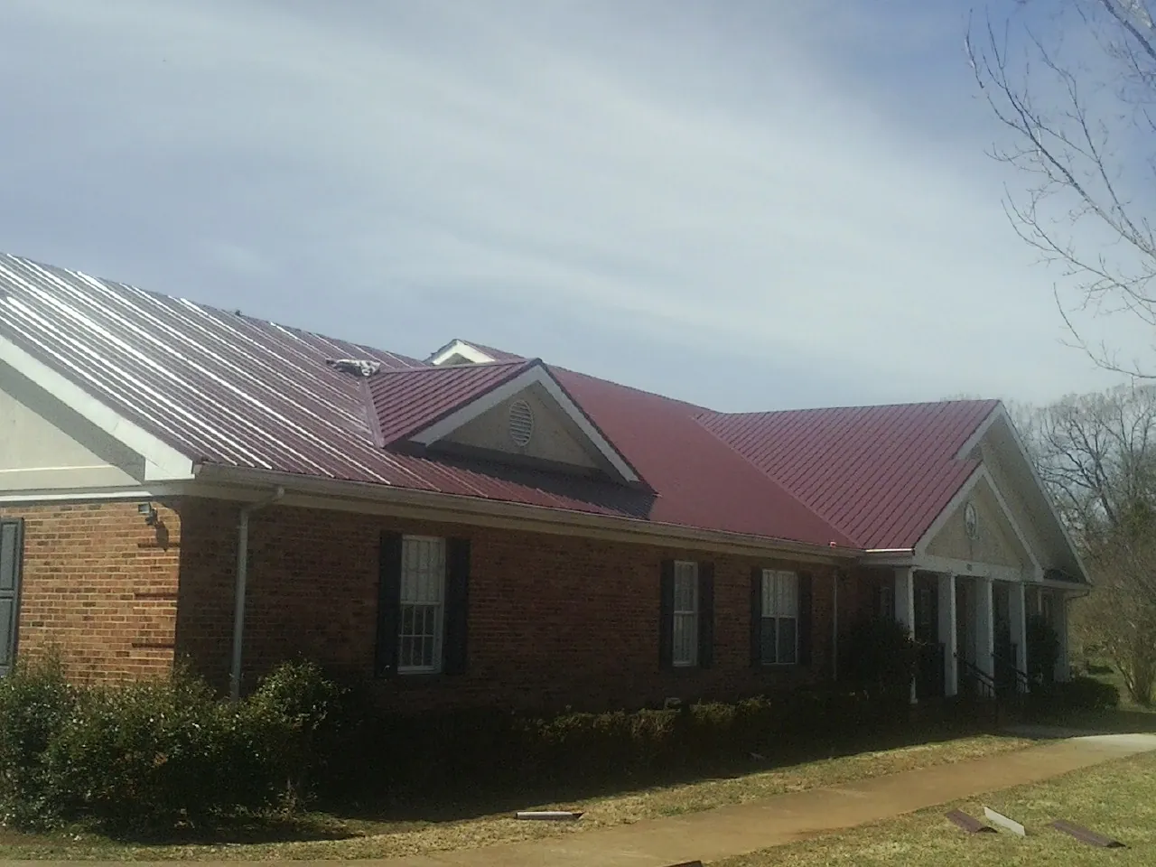 Red metal roof with gabled entries on a long brick building, from a Hail Damage Roof Repair job in Plainsboro