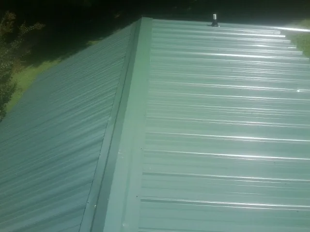 New green metal panels meeting at the ridge of a roof — Flat Roof Repair work by our crew in Plainsboro