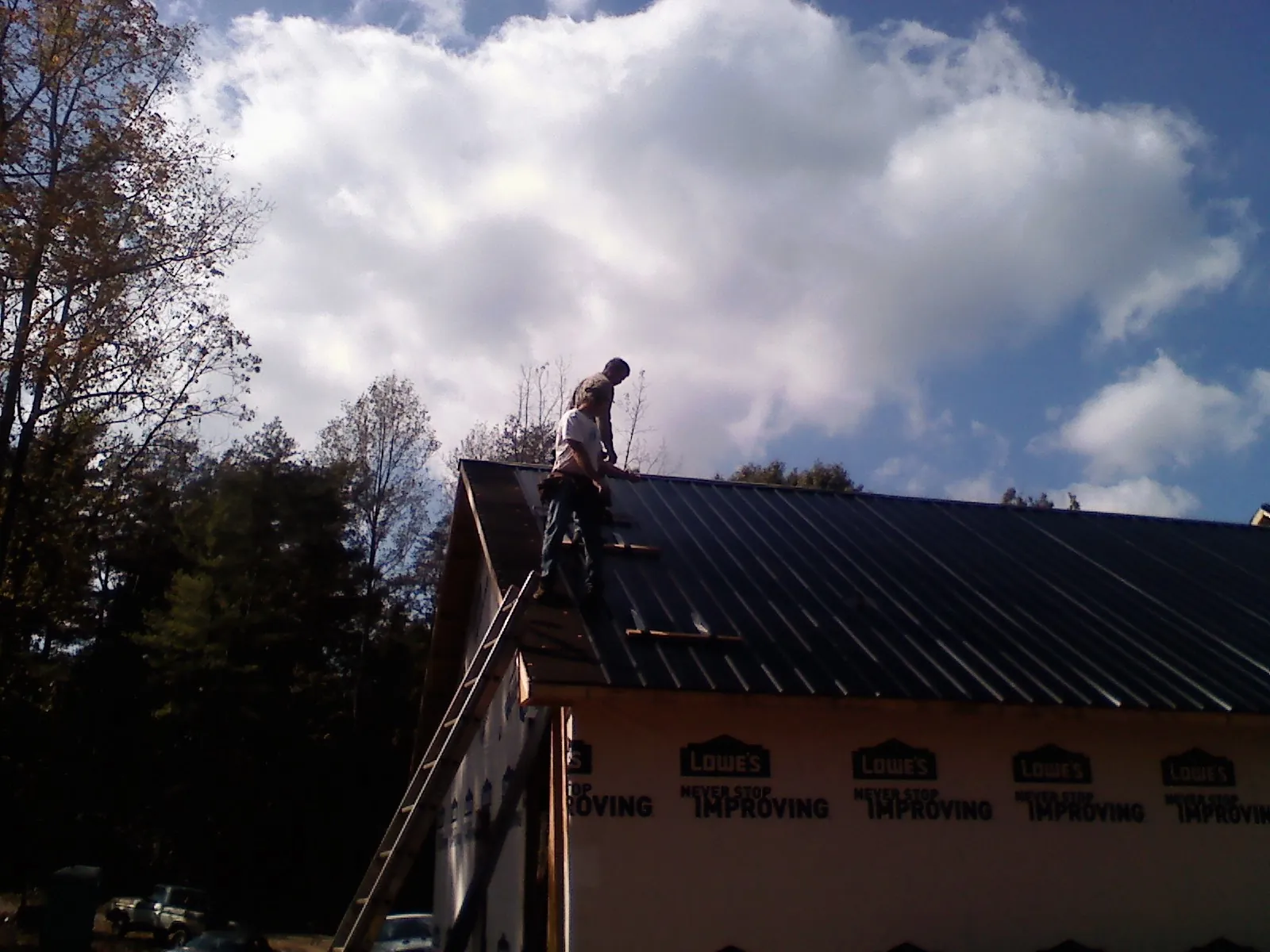 Roofer fastening dark metal panels high against a cloudy sky in Plainsboro