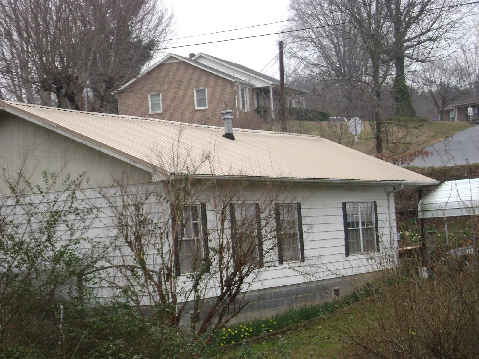 Tan metal roof on a white sided house set into a hillside — Commercial Roofing by Roofing Brothers in Plainsboro